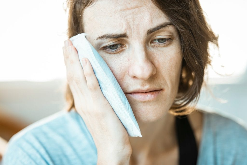 Person holding an ice pack against the cheek during wisdom teeth recovery